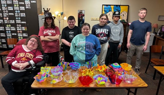 7 high school students stand around a table full of artfully designed acryllic "glass" bowls.