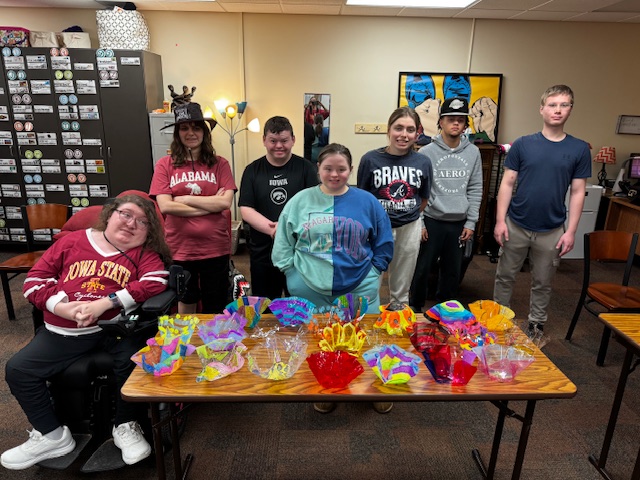 7 high school students stand around a table full of artfully designed acryllic "glass" bowls.